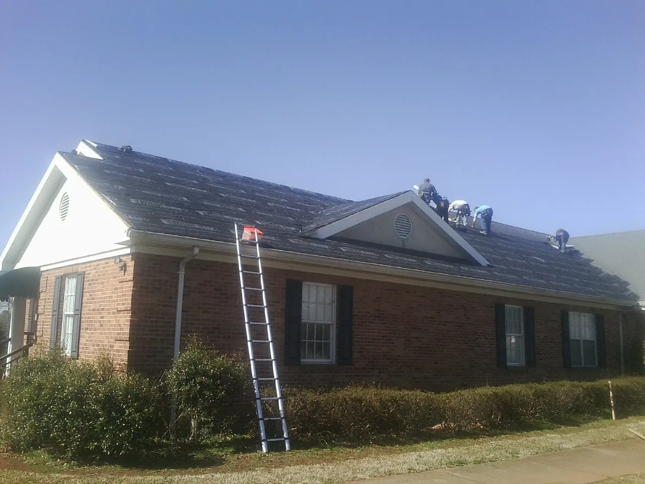 Crew tearing shingles off a brick ranch roof with a ladder set — Emergency Roof Repair work by our crew in Lobelville
