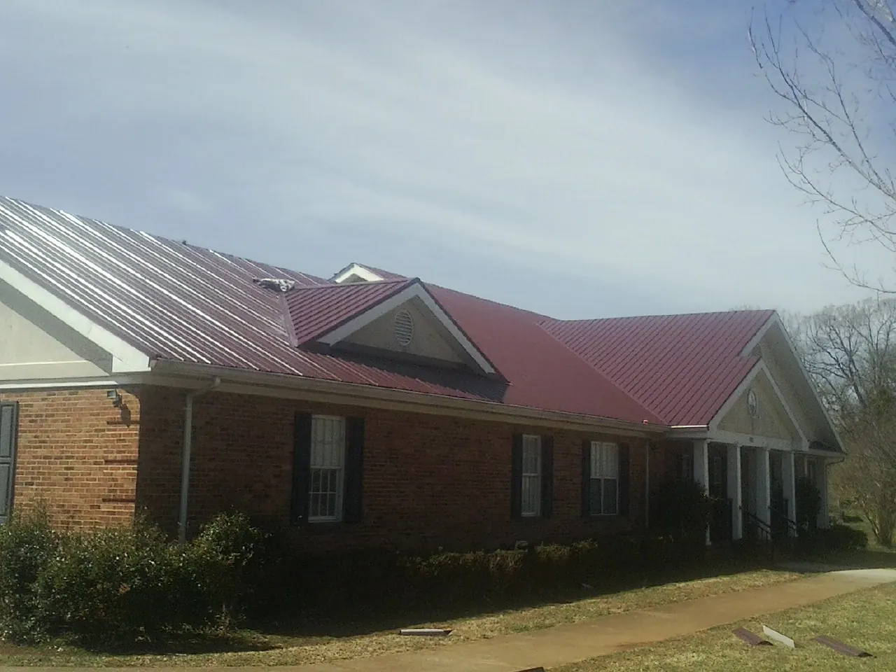 Red metal roof with gabled entries on a long brick building, from a Hail Damage Roof Repair job in Lobelville