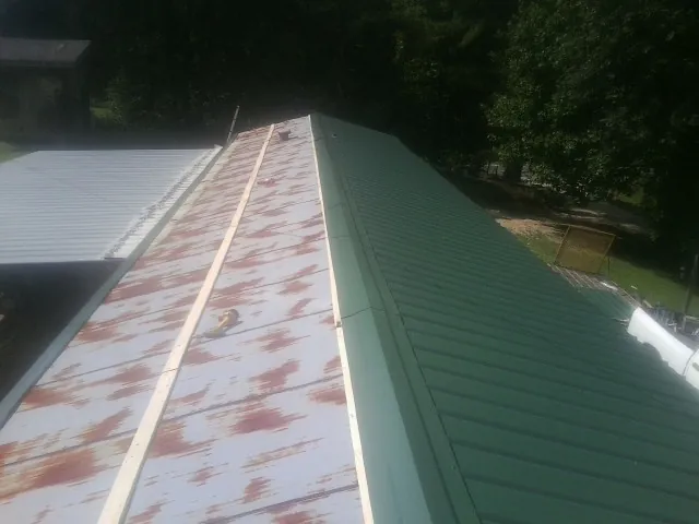 Old rusted panels beside newly installed green metal roofing — Wind Damage Roof Repair by Roofing Brothers in Lobelville