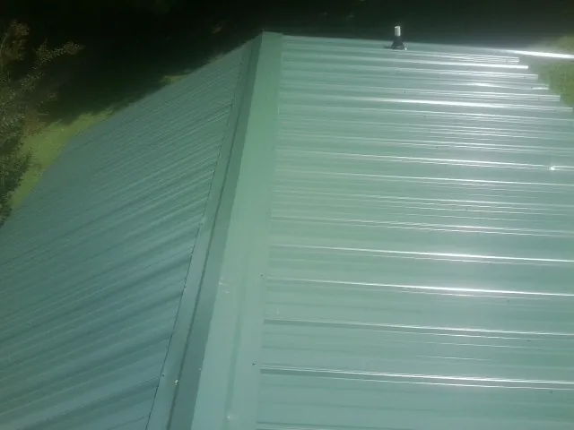 New green metal panels meeting at the ridge of a roof — Flat Roof Repair work by our crew in Lobelville