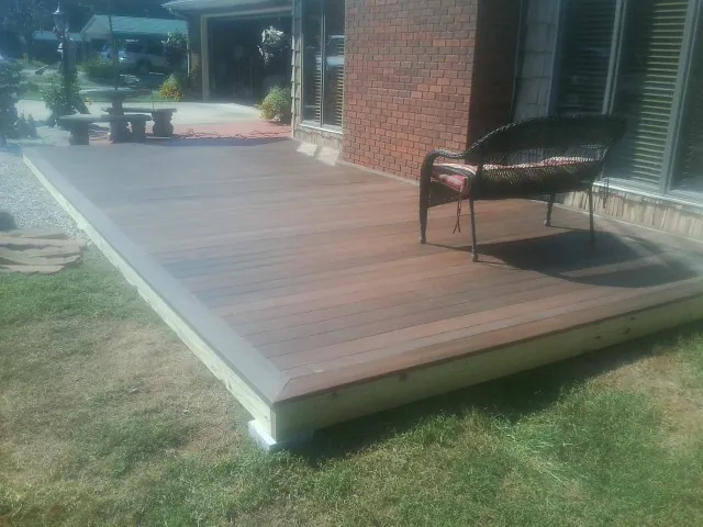 New wood deck and wicker chair beside a brick house in Lobelville