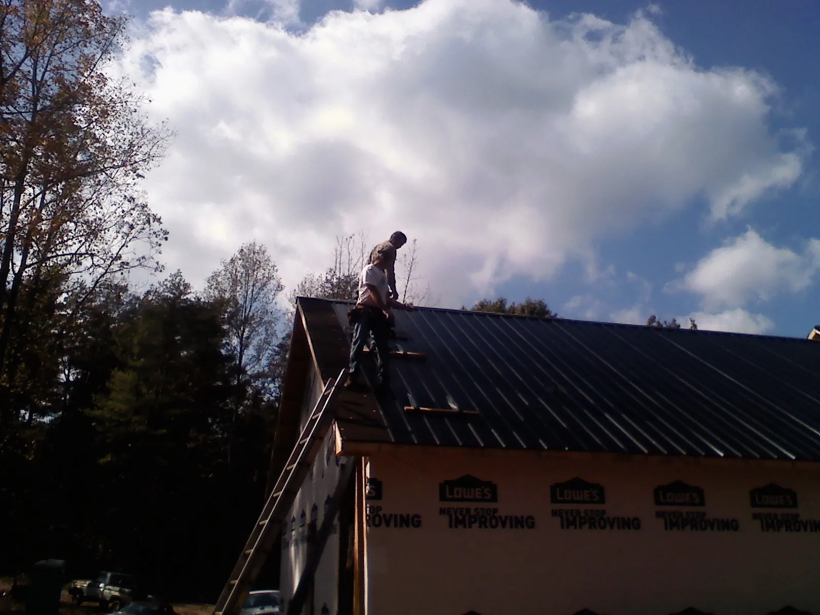 Roofer fastening dark metal panels high against a cloudy sky, from a Roof Inspection job in Lobelville