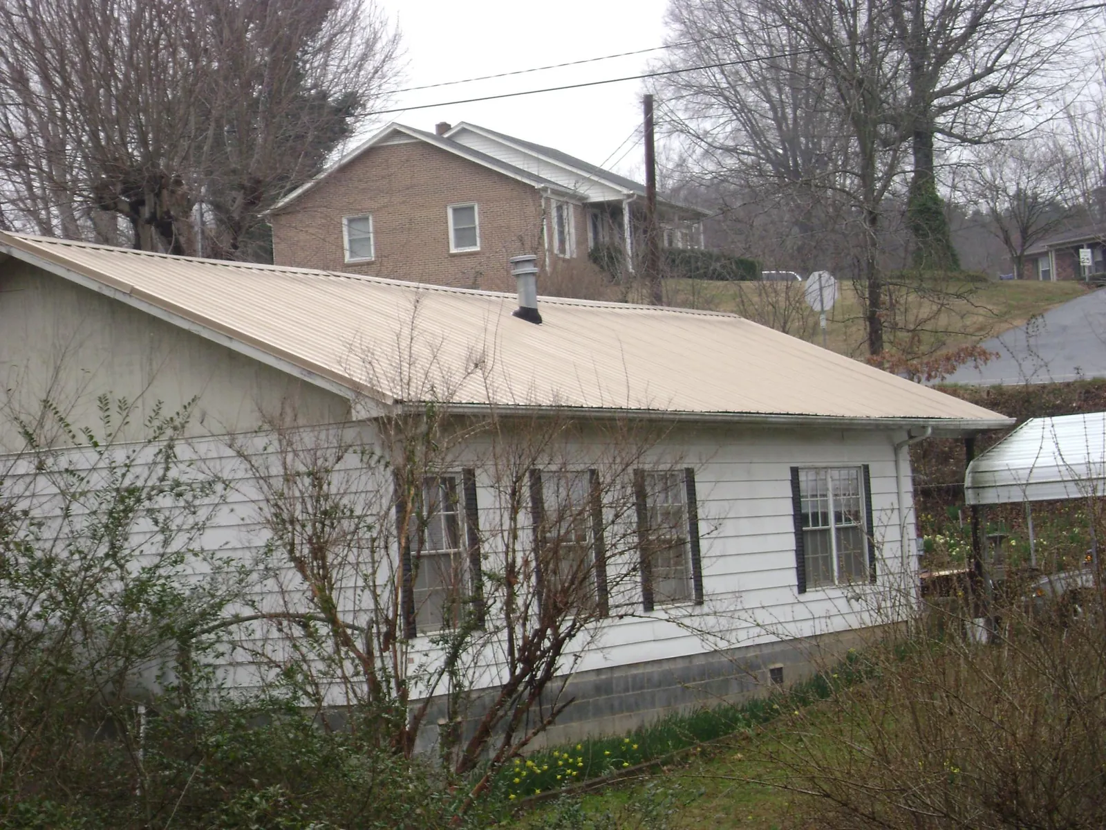 Tan metal roof on a white sided house set into a hillside — Commercial Roofing by Roofing Brothers in Lobelville
