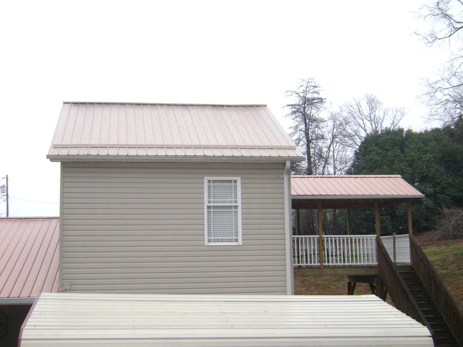 Tan metal roofs on a two story addition and attached porch, from a Roof Replacement job in Lobelville
